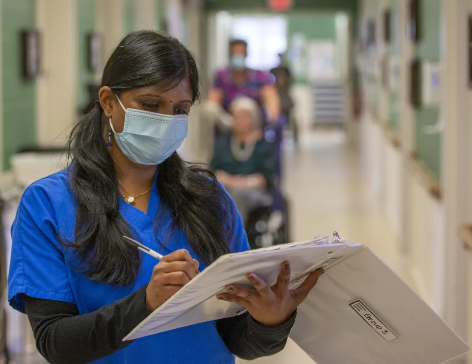 Healthcare worker standing while writing in an open white binder