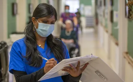 Healthcare worker standing while writing in an open white binder